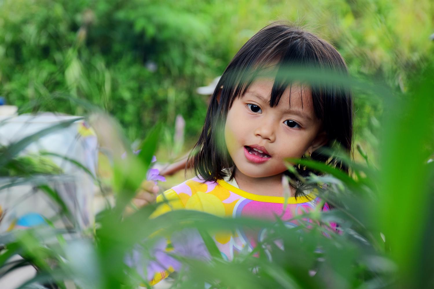 A young girl picks a flower in a wild setting.