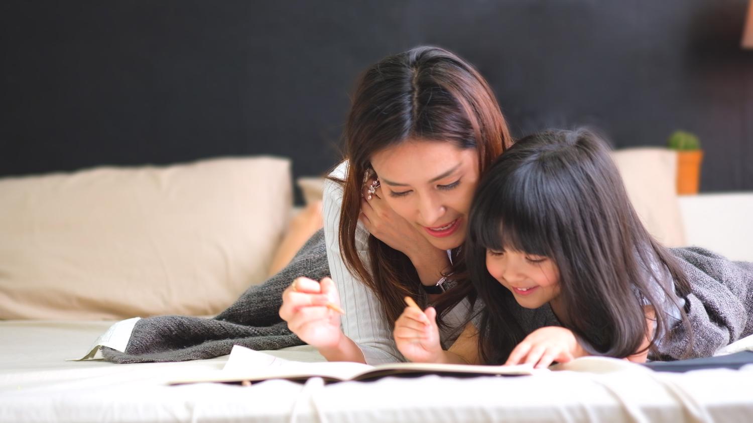 Mom and daughter snuggled together with book and pencil