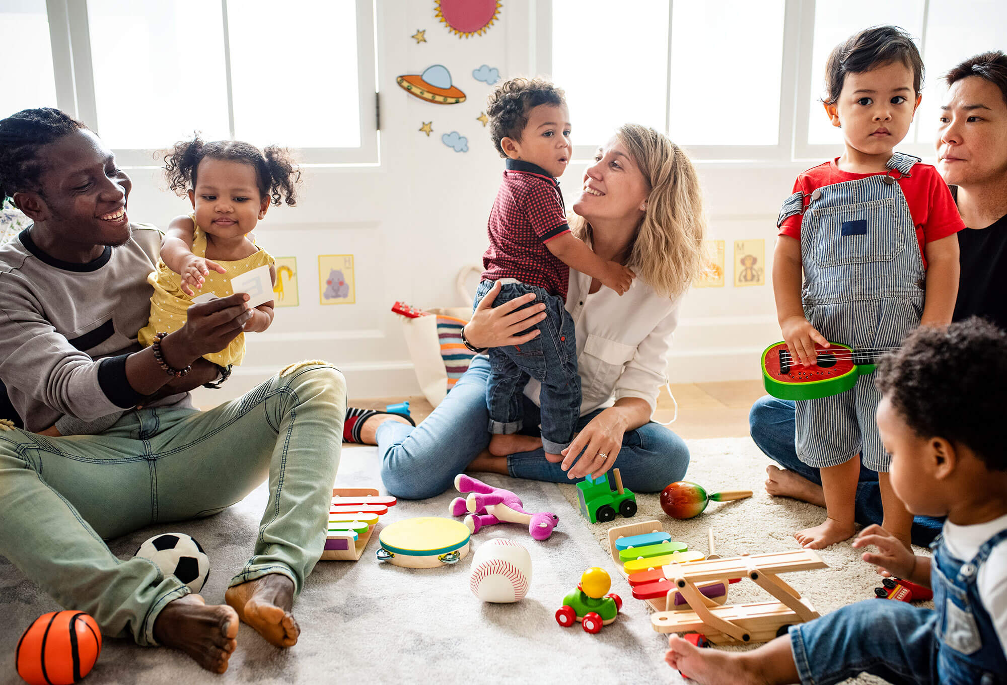 Photo of parents and kids sitting on a floor with lots of toys 